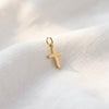 Kleiner goldener Kreuzanhänger mit Öse auf weißem Leinenstoff, polierte Oberfläche, minimalistisches Design