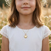Mädchen trägt goldenes Herz-Medaillon Pure Moyen an feiner Kette, weißes Kleid mit Spitze, Blumenkranz im Haar