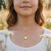 Goldenes Oval-Medaillon Pure Petite an filigraner Kette, getragen von junger Frau mit Blumenkranz im sonnigen Feld