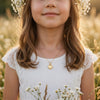 Mädchen trägt goldenes Herz-Medaillon Laurel an filigraner Kette, weißes Kleid mit Spitze, Blumenkranz im Haar