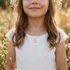 Mädchen trägt goldenes Herz-Medaillon an zarter Kette, weißes Spitzenkleid, Blumenkranz im Haar, sommerliche Wiese