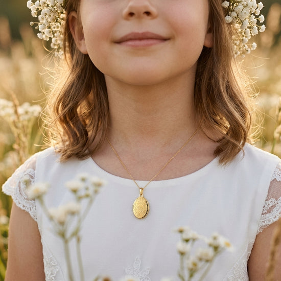 Mädchen mit goldenem Oval-Medaillon Peony an zarter Kette, weißes Kleid mit Spitze, Blumenkranz im Haar