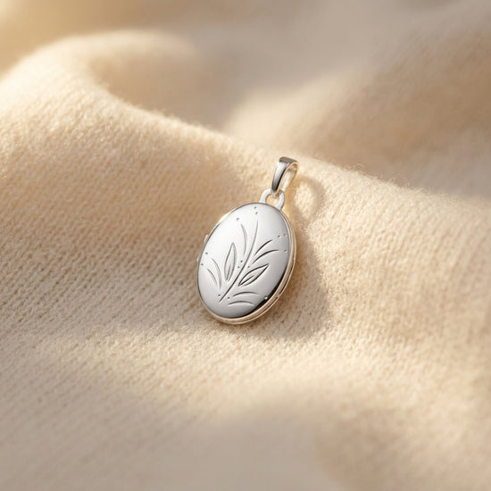 Silbernes ovales Medaillon mit graviertem Blättermotiv auf cremefarbenem Stoff, Anhänger aus 925er Sterlingsilber
