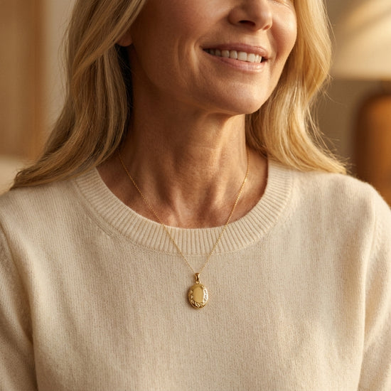 Frau trägt goldenes Oval-Medaillon Ivy mit zartem Blattdekor an feiner Kette über cremefarbenem Pullover