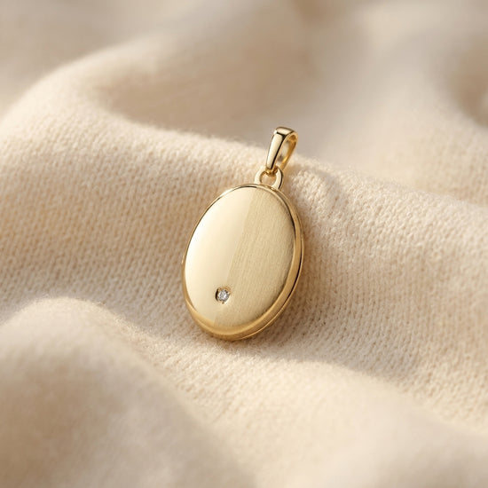 Goldenes ovales Medaillon mit kleinem Zirkonia-Stein, auf cremefarbenem Stoff drapiert