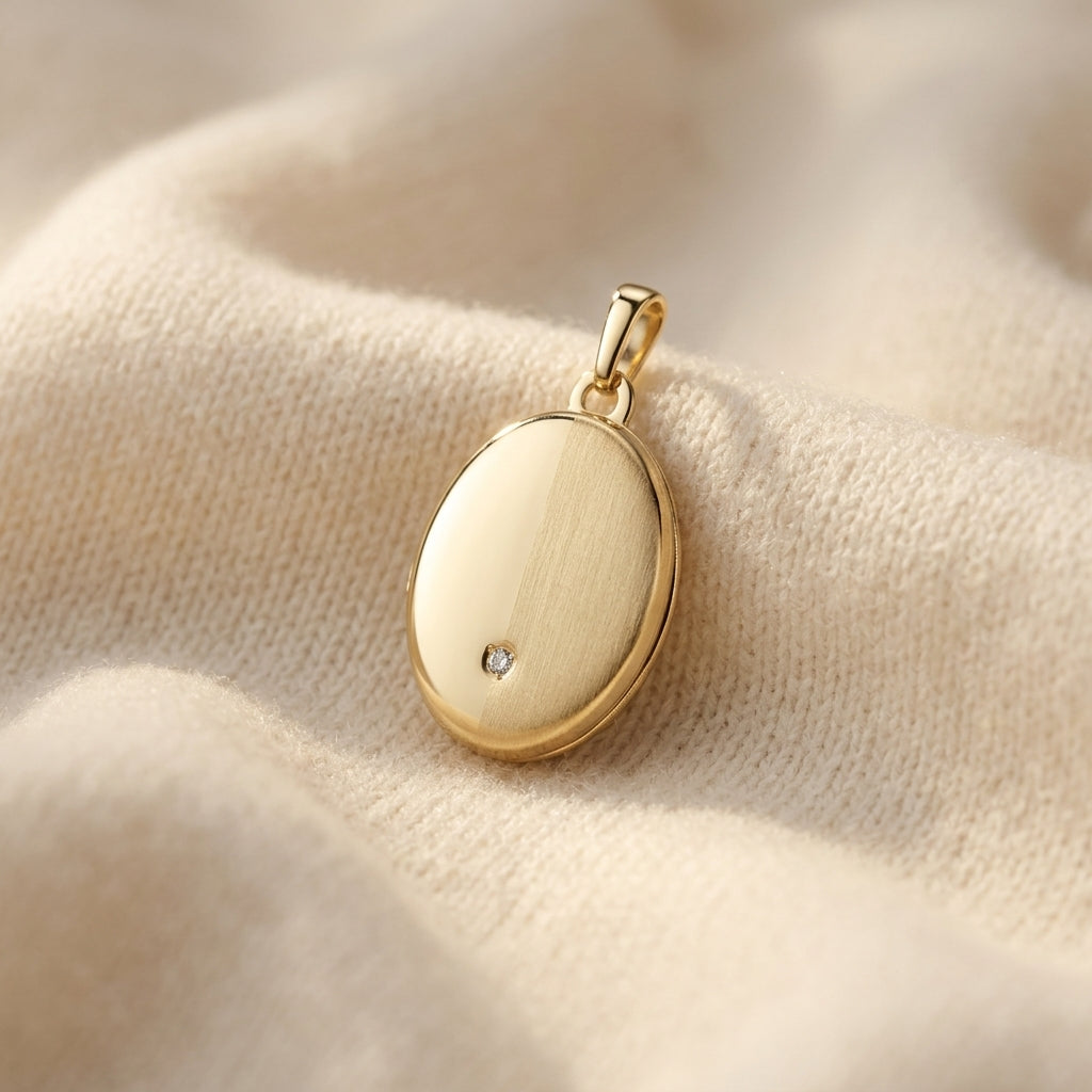 Goldenes ovales Medaillon mit kleinem Zirkonia-Stein, auf cremefarbenem Stoff drapiert