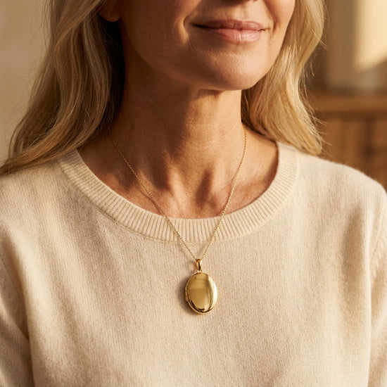 Frau trägt goldenes Oval-Medaillon Pure Moyen an feiner Kette über beigem Pullover, polierte Oberfläche