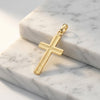 Goldener Kreuz-Anhänger mit feiner Strukturierung in der Mitte, auf weißem Marmor präsentiert