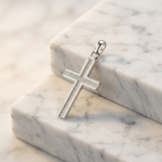 Silberner Kreuz-Anhänger mit glitzernder Mittellinie auf weißem Marmor, polierte Oberfläche mit Öse