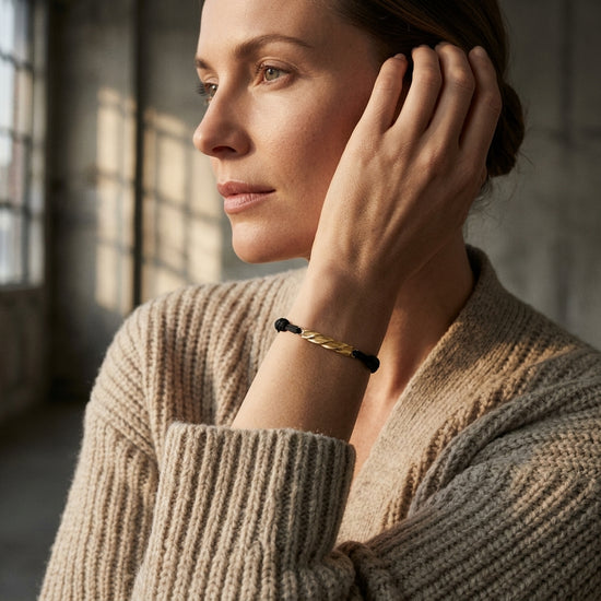 Frau trägt Breeze small Armband mit goldener Kette und schwarzen Details am Handgelenk, beige Strickpullover