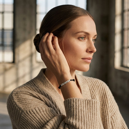 Frau mit beigem Strickpullover trägt filigranes Silberarmband Breeze small am Handgelenk, Profil vor Fensterlicht