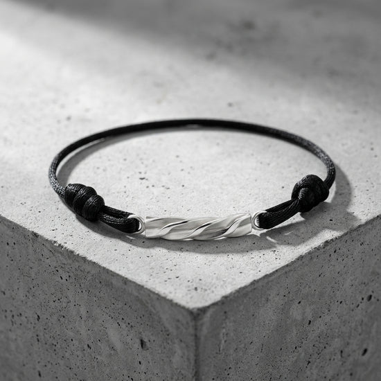Schwarzes Textilarmband mit gedrehtem Silberelement, minimalistisches Design auf grauem Betonuntergrund