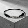 Schwarzes Textilarmband mit gedrehtem Silberelement, minimalistisches Design auf grauem Betonuntergrund