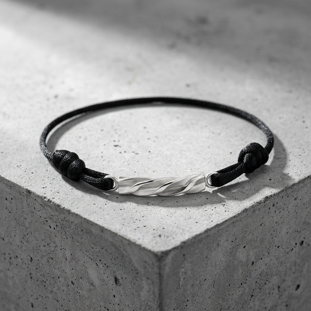 Schwarzes Textilarmband mit gedrehtem Silberelement, minimalistisches Design auf grauem Betonuntergrund