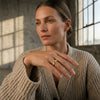 Frau trägt goldenen Ring Breeze mit wellenförmigem Design am Ringfinger, beige Strickpullover, natürliches Licht