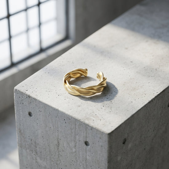Goldener Ring Breeze mit gedrehtem Wellendesign auf grauem Betonblock, offene Ringform, handgefertigt von Aurevia