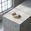 Goldener Ring Breeze mit gedrehtem Wellendesign auf grauem Betonblock, offene Ringform, handgefertigt von Aurevia