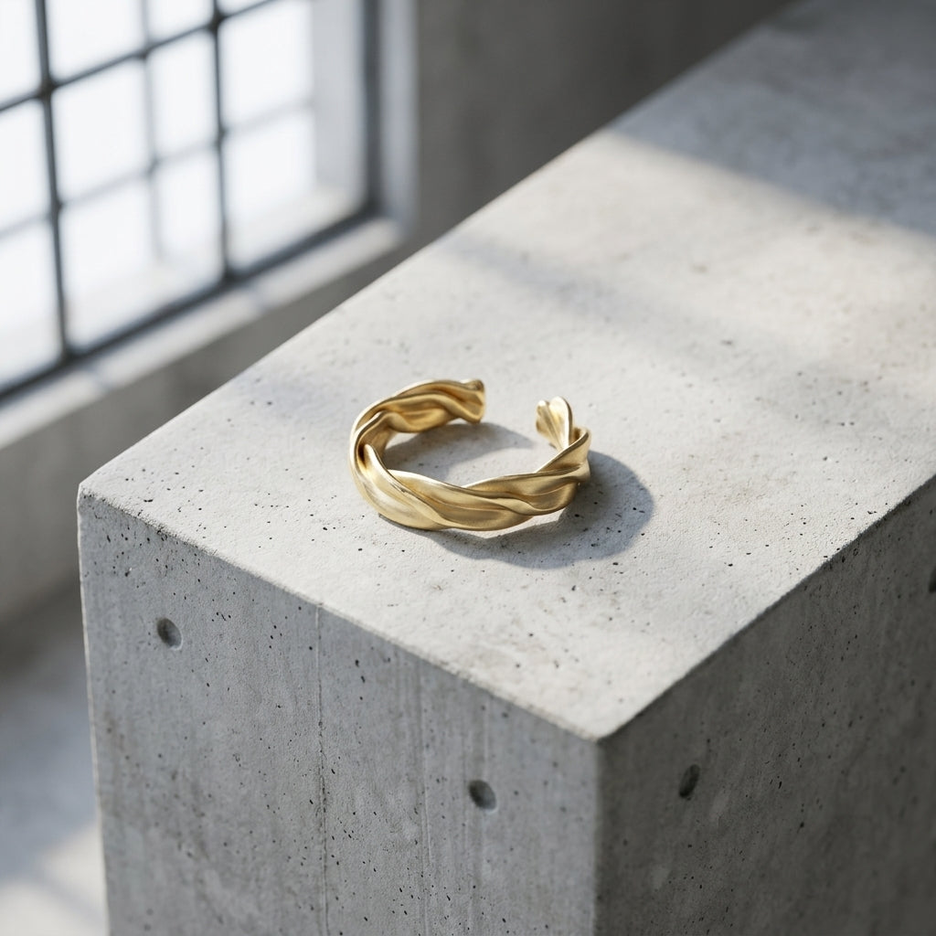 Goldener Ring Breeze mit gedrehtem Wellendesign auf grauem Betonblock, offene Ringform, handgefertigt von Aurevia