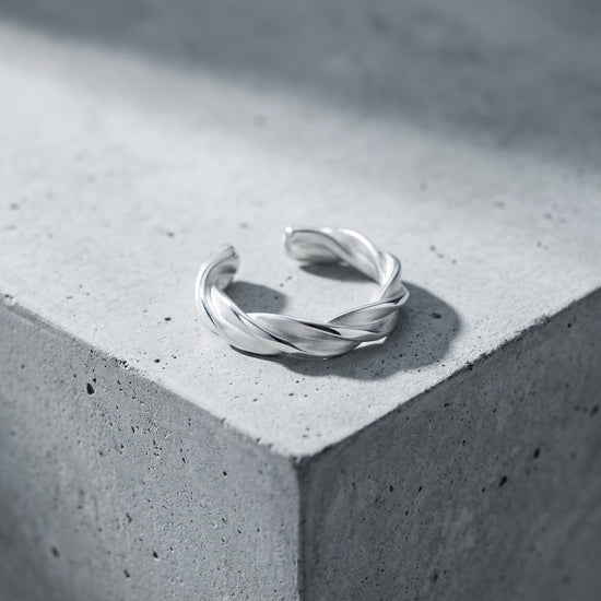 Silberner Ring Breeze mit gedrehtem Design auf grauer Betonoberfläche, offene Form, handgefertigt aus 925er Sterlingsilber