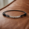 Schwarzes Lederarmband mit gedrehtem Silberelement als Mittelteil auf braunem Leder