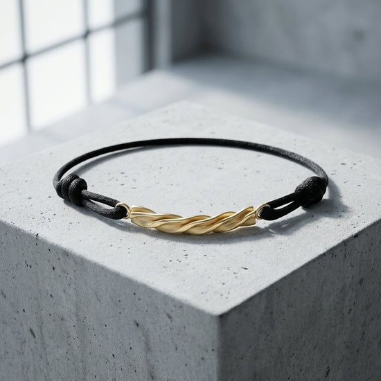 Schwarzes Lederarmband mit goldener gedrehter Spirale als Mittelelement auf grauem Betonwürfel