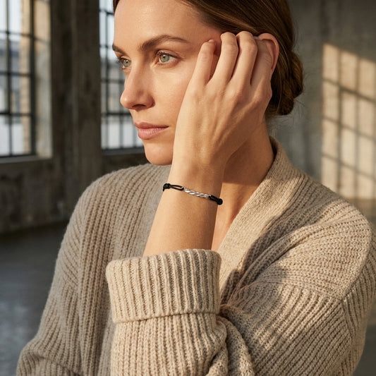 Frau trägt schwarzes Breeze Armbändchen mit silbernen Akzenten aus Edelmetall am Handgelenk, beiger Strickpullover