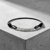 Schwarzes Textilarmband mit gedrehtem Silberelement in der Mitte, auf grauem Betonwürfel präsentiert