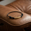 Schwarzes Textilarmband mit gedrehtem Goldelement auf braunem Ledersofa, handgefertigt von Aurevia