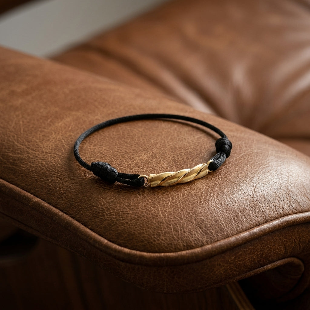 Schwarzes Textilarmband mit gedrehtem Goldelement auf braunem Ledersofa, handgefertigt von Aurevia