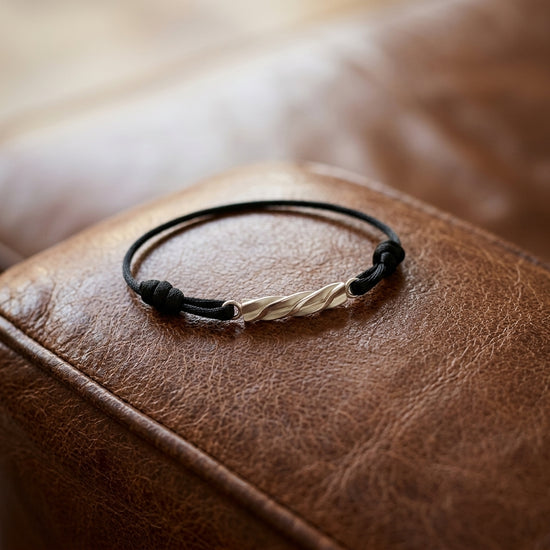 Schwarzes Lederarmband mit gedrehtem Goldverschluss auf brauner Ledertasche, handgefertigt von Aurevia