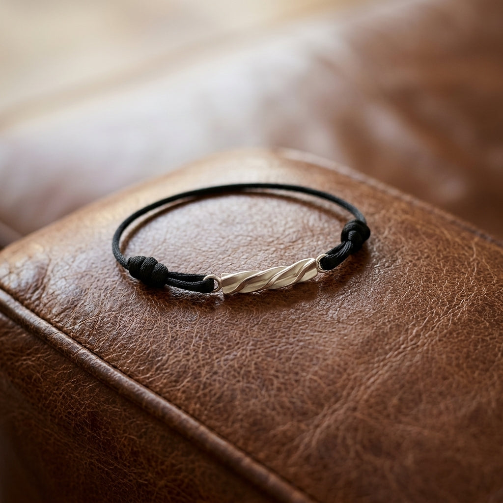 Schwarzes Lederarmband mit gedrehtem Goldverschluss auf brauner Ledertasche, handgefertigt von Aurevia