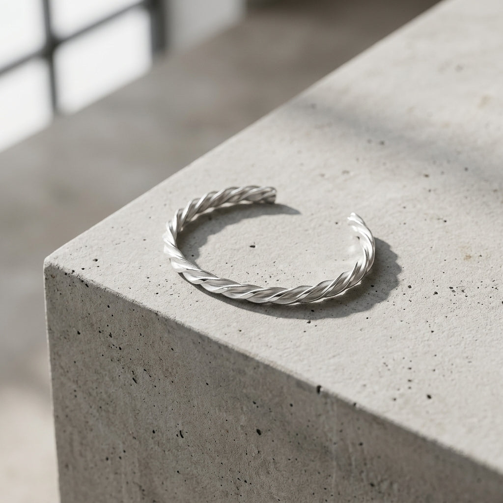 Offener Silberarmreif Breeze mit gedrehter Struktur auf Betonblock, minimalistisches Design aus massivem Sterlingsilber