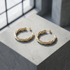 Goldene Creolen mit gedrehter Struktur auf hellem Steinblock, natürliches Licht wirft sanfte Schatten