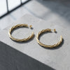 Goldene Creolen mit gedrehter Struktur auf grauem Stein, handgefertigt aus echtem Gold, Aurevia Breeze large