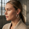 Frau im Profil trägt große, gedrehte Silber-Creolen Breeze large von Aurevia, beige Strickjacke, natürliches Licht