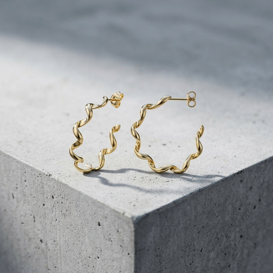 Goldene Helix-Creolen mit gedrehter Spiralform aus massivem Edelmetall, auf hellem Betonwürfel präsentiert