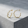 Goldene Helix-Creolen mit gedrehter Spiralform aus massivem Edelmetall, auf hellem Betonwürfel präsentiert