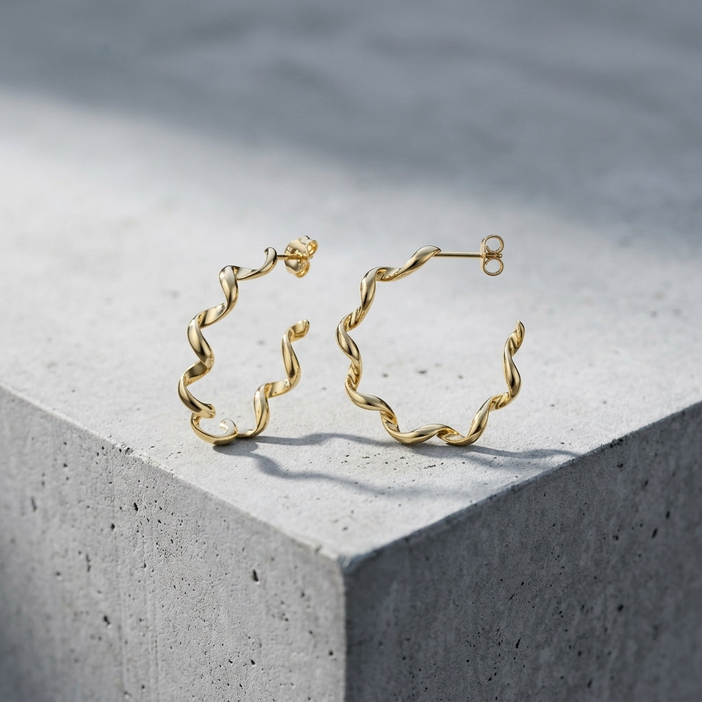 Goldene Helix-Creolen mit gedrehter Spiralform aus massivem Edelmetall, auf hellem Betonwürfel präsentiert