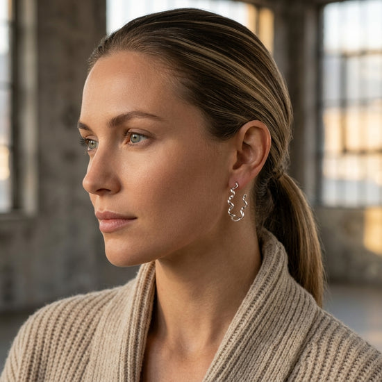Frau im Profil trägt silberne Helix-Creolen mit gewelltem Design aus Edelmetall, schlicht-eleganter Look
