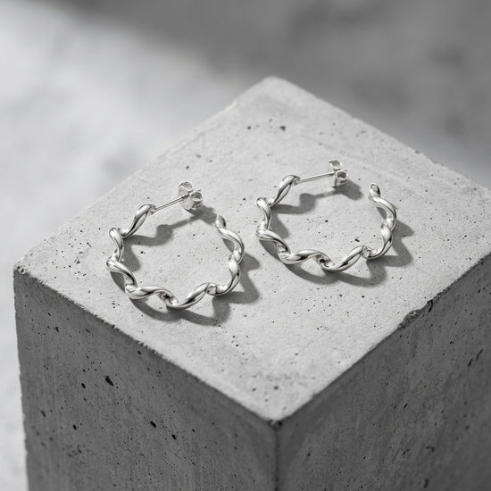 Silberne Helix-Creolen mit gedrehter Struktur auf grauem Betonblock, Aurevia Manufaktur