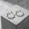 Silberne Helix-Creolen mit gedrehter Struktur auf grauem Betonblock, Aurevia Manufaktur