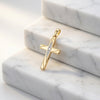 Goldener Kreuz-Anhänger Flow mit diagonalem Zirkonia-Band auf weißen Marmorstufen