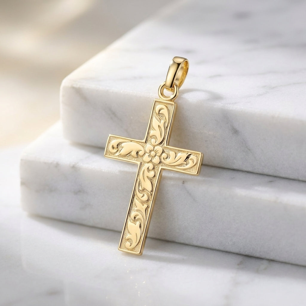 Goldener Kreuz-Anhänger mit floralen Gravuren und Blüte in der Mitte, auf weißem Marmor
