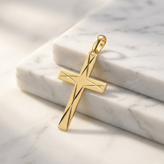 Goldener Kreuz-Anhänger mit diagonaler Liniengravur auf weißem Marmor, Edelmetall aus Pforzheimer Manufaktur
