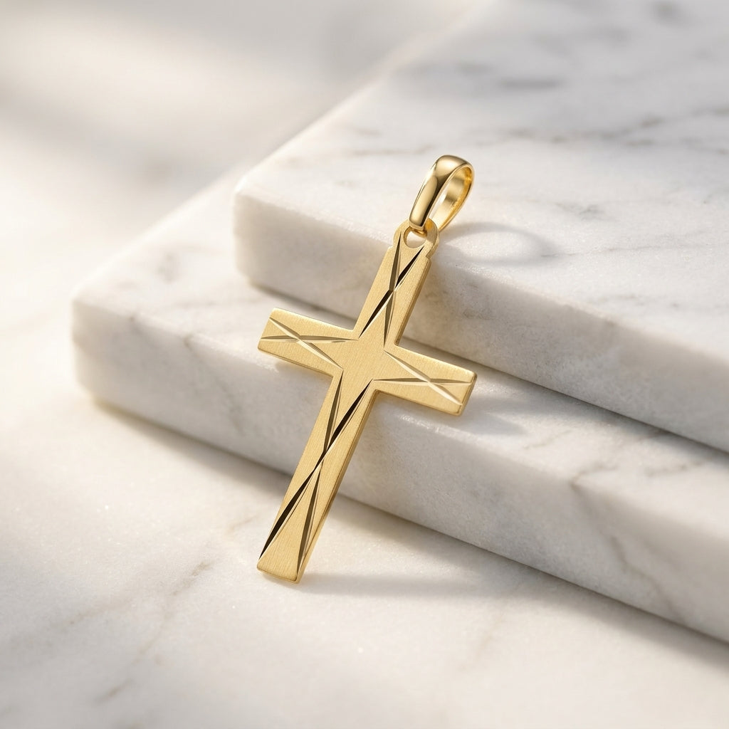 Goldener Kreuz-Anhänger mit diagonaler Liniengravur auf weißem Marmor, Edelmetall aus Pforzheimer Manufaktur