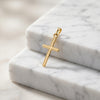 Goldener Kreuz-Anhänger Centro mit feiner Linienstruktur auf weißen Marmorblöcken