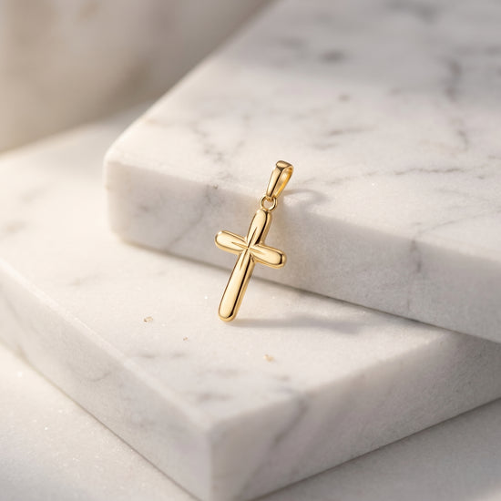 Goldener Kreuz-Anhänger mit glatter, abgerundeter Oberfläche auf weißem Marmor, handgefertigt aus massivem Gelbgold