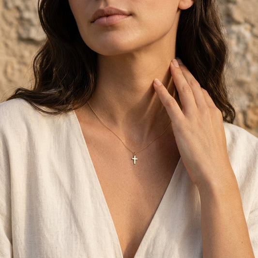 Frau trägt goldenen Kreuz-Anhänger Essence Mini an filigraner Kette, weißes Leinenhemd, natürliches Sonnenlicht