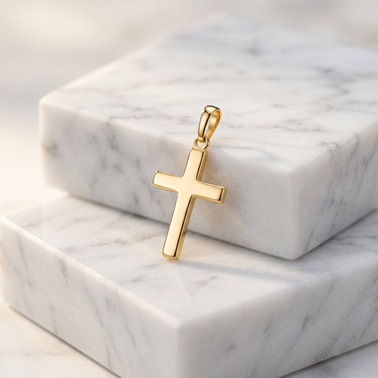 Goldener Kreuz-Anhänger Essence Moyen auf weißem Marmor, polierte Oberfläche, minimalistisches Design