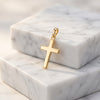 Goldener Kreuz-Anhänger Essence Moyen auf weißem Marmor, polierte Oberfläche, minimalistisches Design